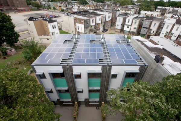 Modern, sustainable multifamily housing; ariel shot showing solar panels on roof, trees and rowhomes surrounding