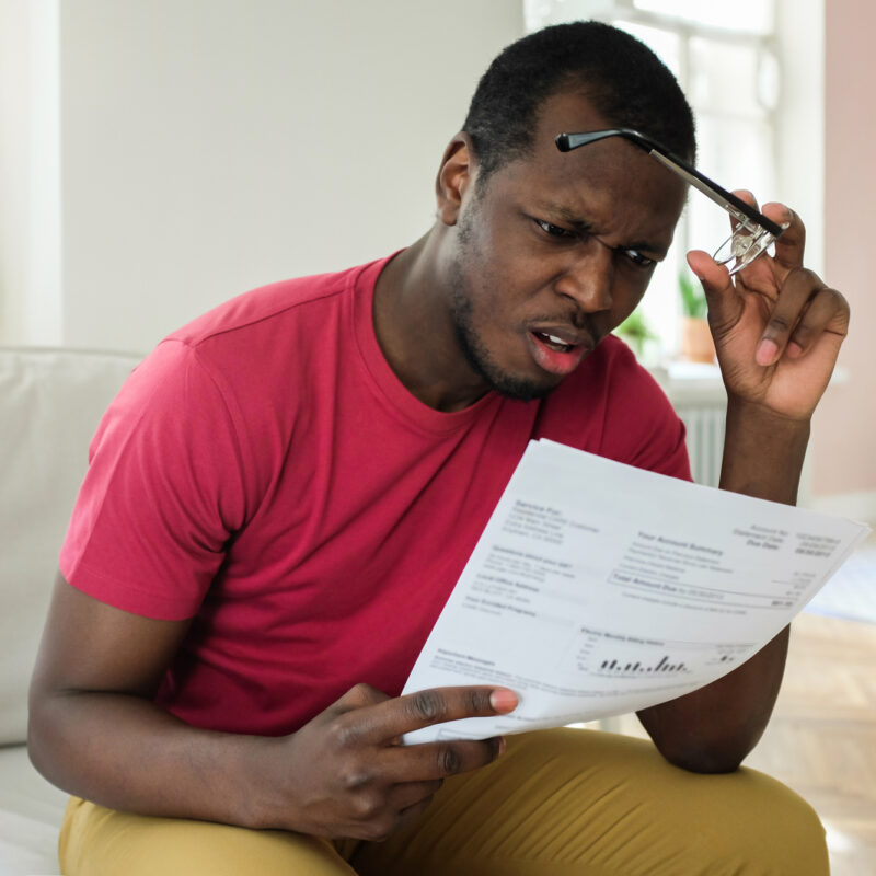 Shocked sad young man surprised and stressed as read utility bill, holding eyeglasses