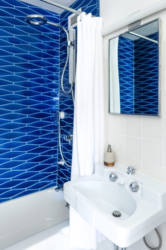 interior image of bathroom sink, mirror, and curtained shower; shower shows brilliant blue tile work and ring shower wand - photo