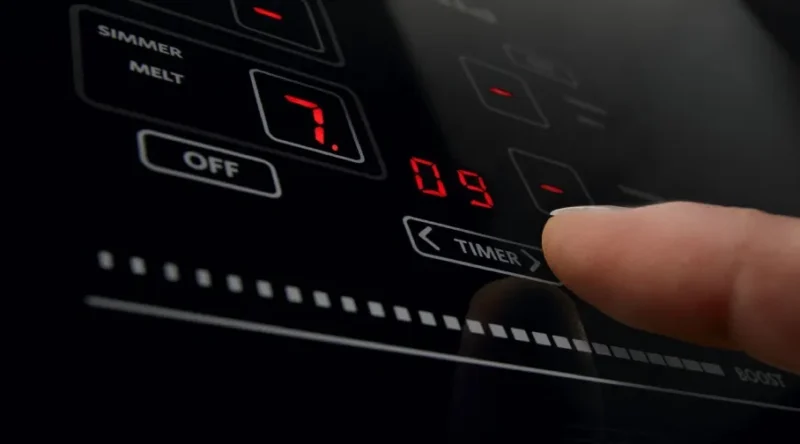 Closeup of touch control panel of induction stove; index finger is adjusting timer - photo