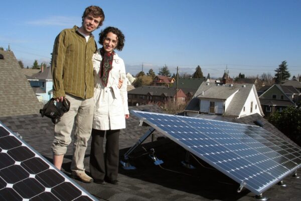 Man and woman stand closely together on home's roof with solar panels - photo