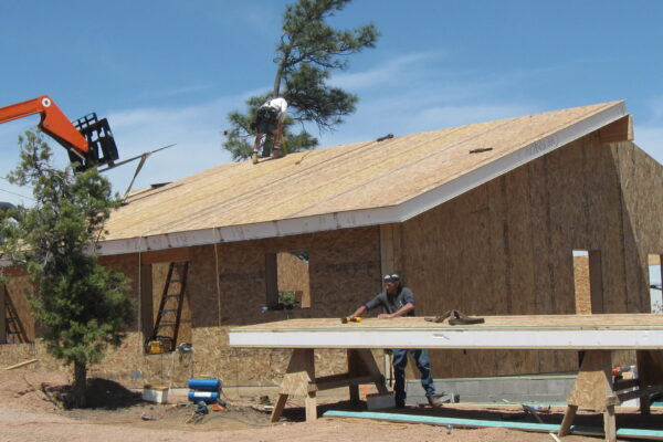 exterior of SIP home under construction; crane and workmen place roof panels – photo