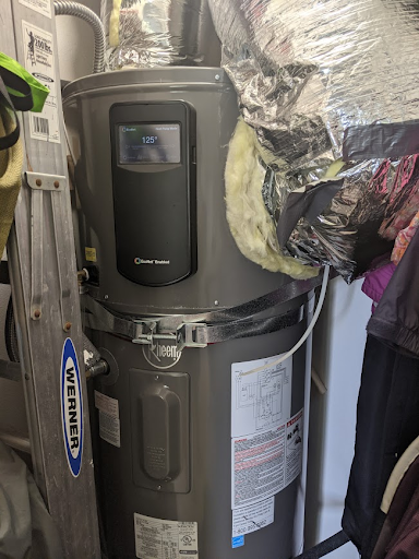 heat pump water heater installed in residential closet surrounded by various tools and clothing items - photo