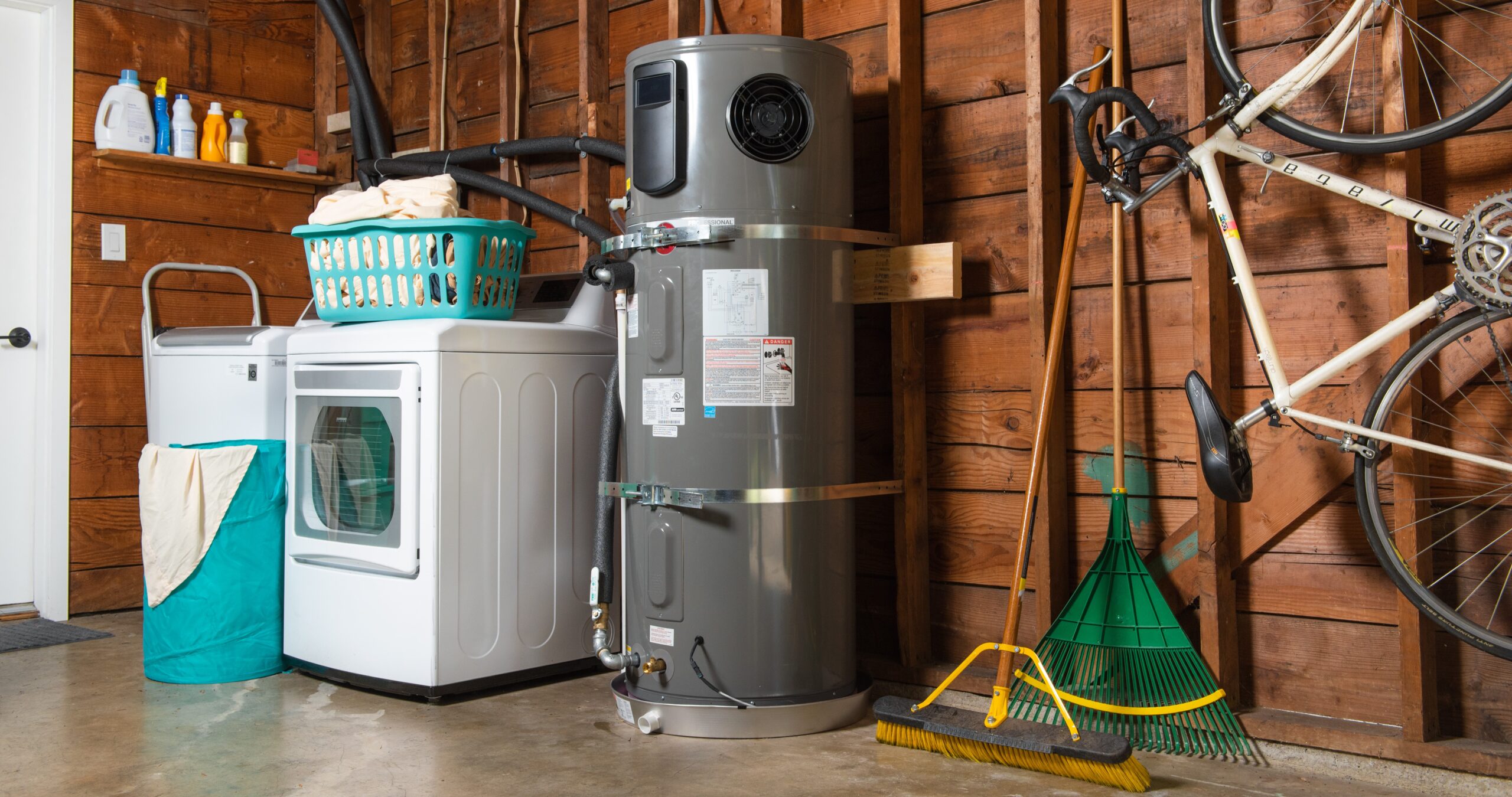 Interior viewe of residential garage housing washer/dryer, heat pump water heater bicycle and gardening tools - photo
