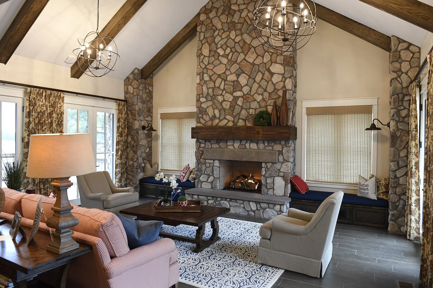 interior view of SIP home shows large stone fireplace with crackling fire, high pitched ceiling with wooden beams, cosy furnishings and windows on both sides; unique metal chandeliers and sconces - photo