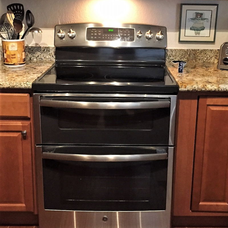 Black and stainless oven and range, Certified by ENERGY STAR, stands between kitchen counters and cabinets; counter holds decorative items and untensils/appliance - photo
