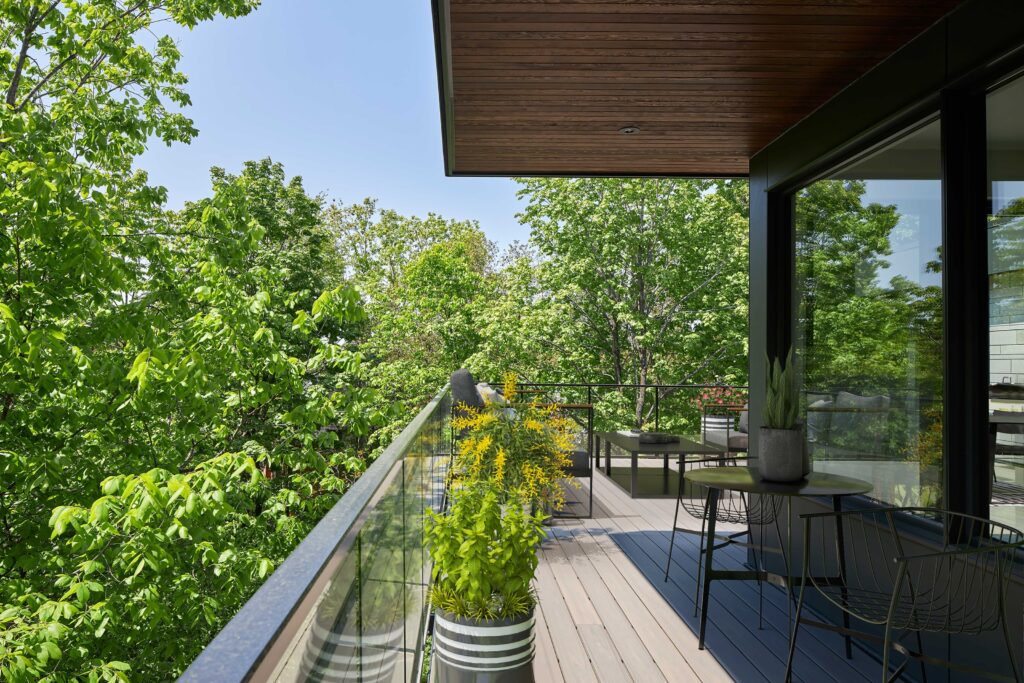 view off terrace of modern net zero home shows awning above and leafy woods - photo