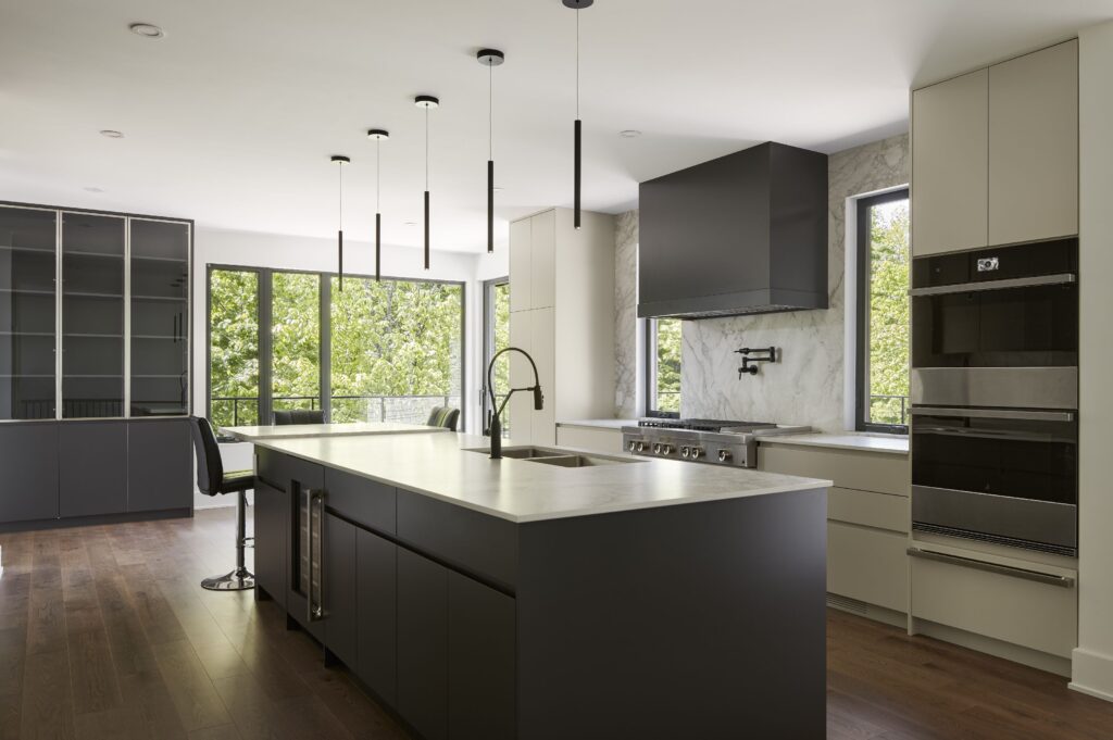 Interior view of modern kitchen of net zero home with cylinder pendant lights, island with sink, and view to outdoors - photo