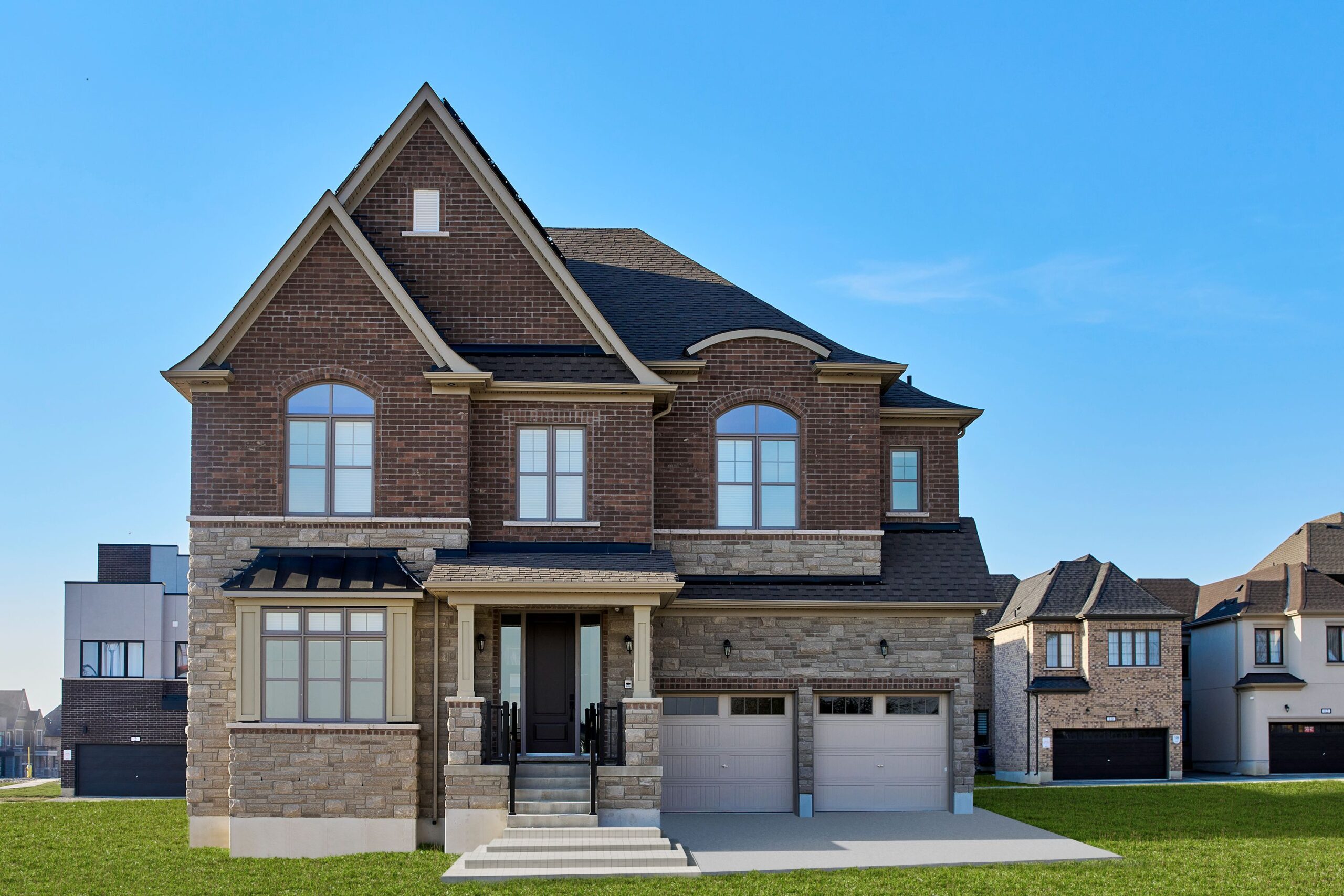 street view of lovely net zero home with ston and brick facade against a blue sky - photo